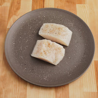 Two halibut filets on plate with seasoning sprinkled on top.